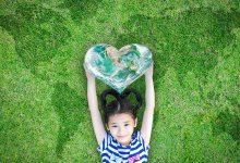 Young girl lying down, smiling, in the grass with heart-shaped globe above her head.