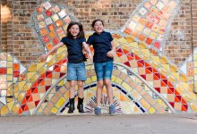 Two girls jumping up in front of a large tiled wall of a sun